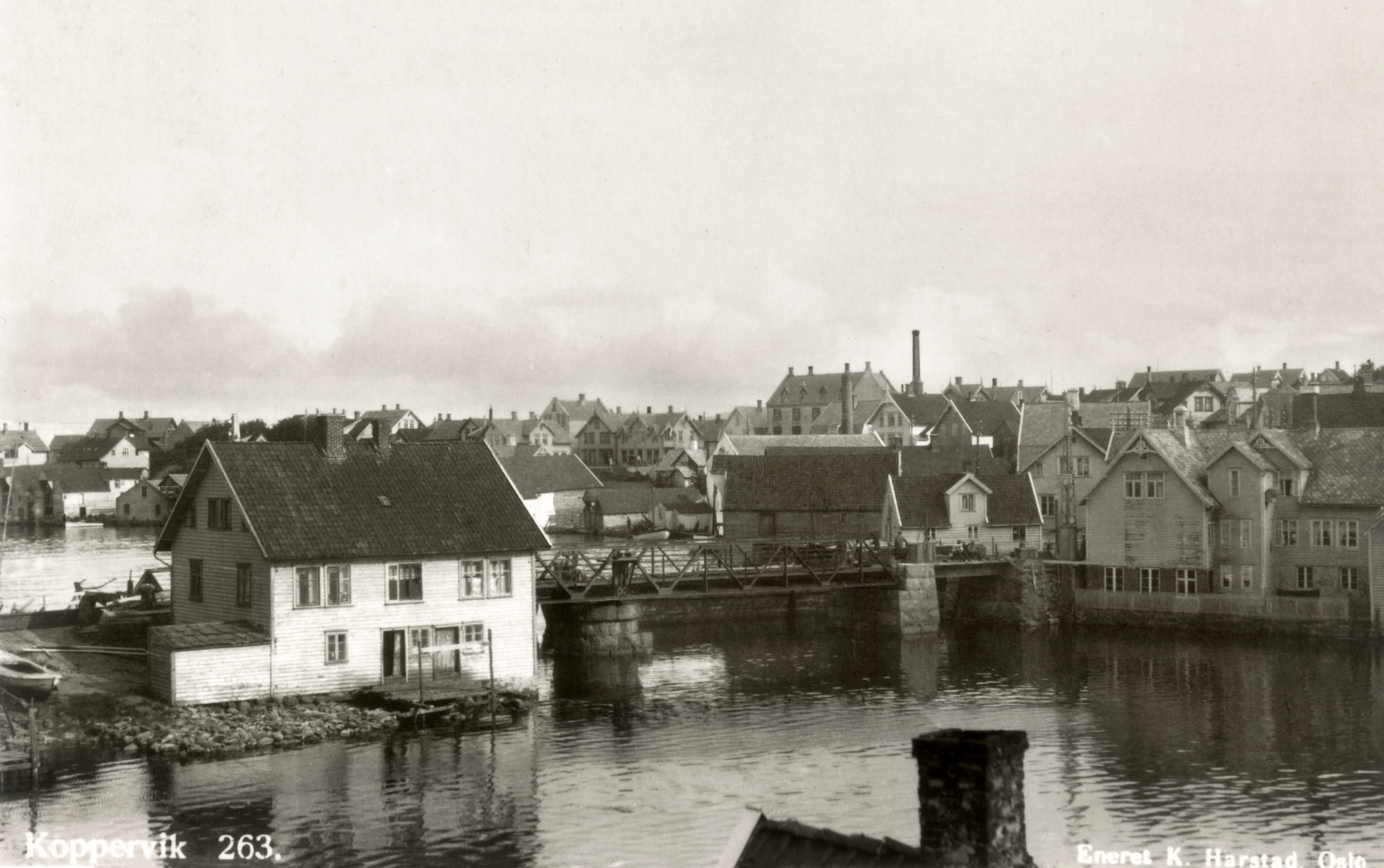 Kopervik havn innenfor Strømsund bro Hophuset til venstre for broen og Knutsen/Talgø til høyre. Skorsteinene til South Norway hermetikkfabrikk/Karmøy Veveri og Lundbergs bakeri ... Bilde er tatt 1929 og viser ferdigstillelse av ny bro . En lekter skimtes på utsiden av broen , denne ble brukt som midlertidig vei under byggingen av broen