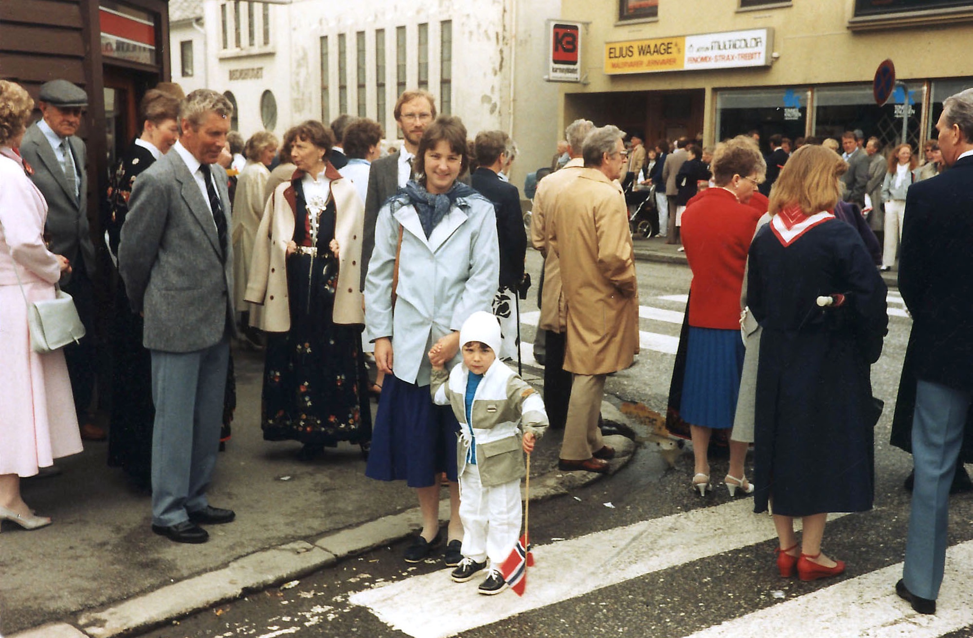 17. mai i Kopervik Folk venter på toget i krysset Hovedgaten og Skudenesvegen ...  Bl.a.: Arnulf Thorvaldsen, Klaudia Lundberg, Anders Lundberg, fru Anders Lundberg og Knut og Haldis Frøiland Jensen med ryggen til