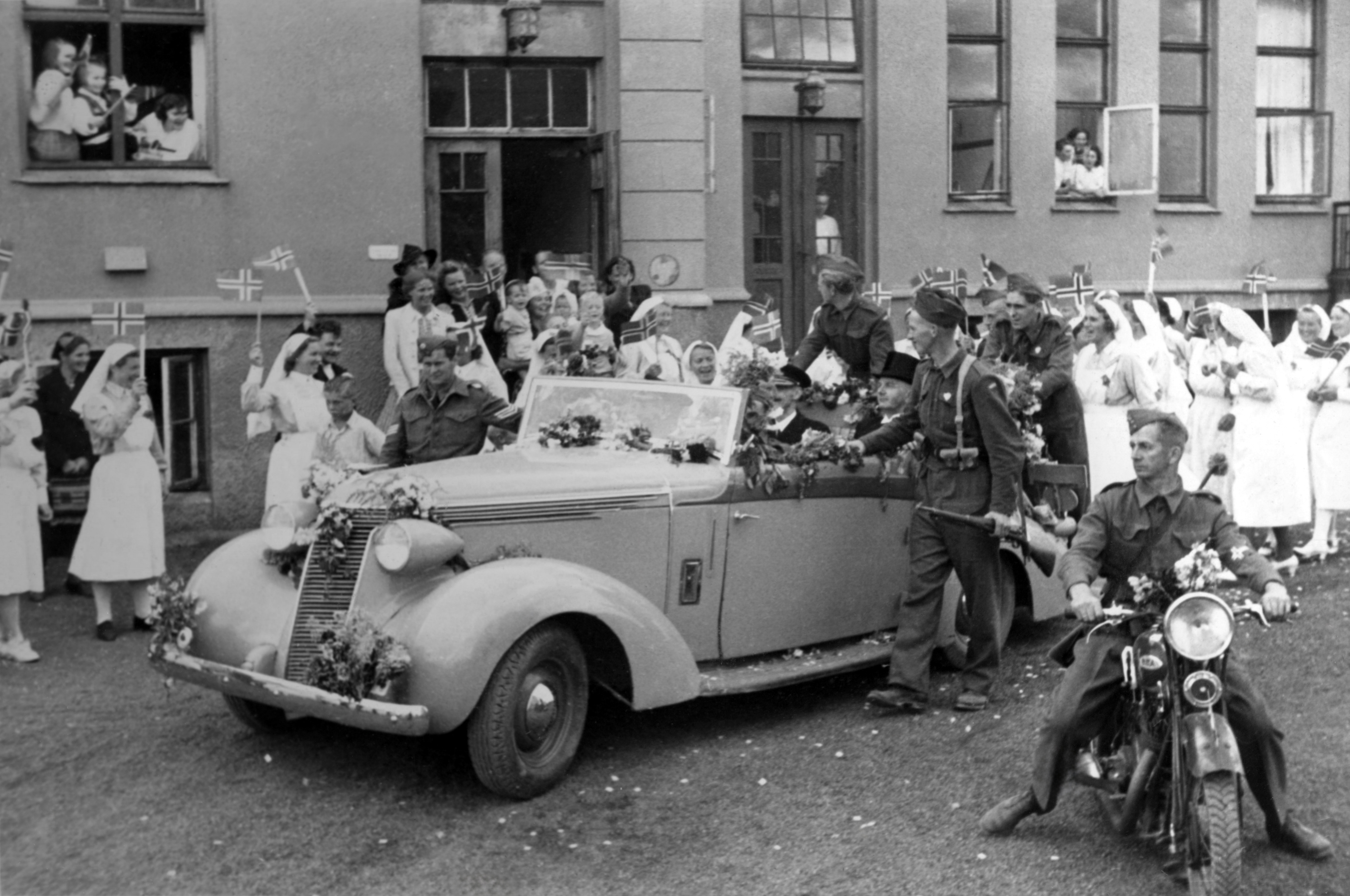 Haugesund sykehus 22 august 1945, Kong Haakon Besøker Haugesund, Haugesund ordfører Christian Haaland sitter også i bilen. Trygve Håvarstein på venstre side av bilen og Harald Mikkelsen bak på bilen som vakter, begge to fra Kopervik.