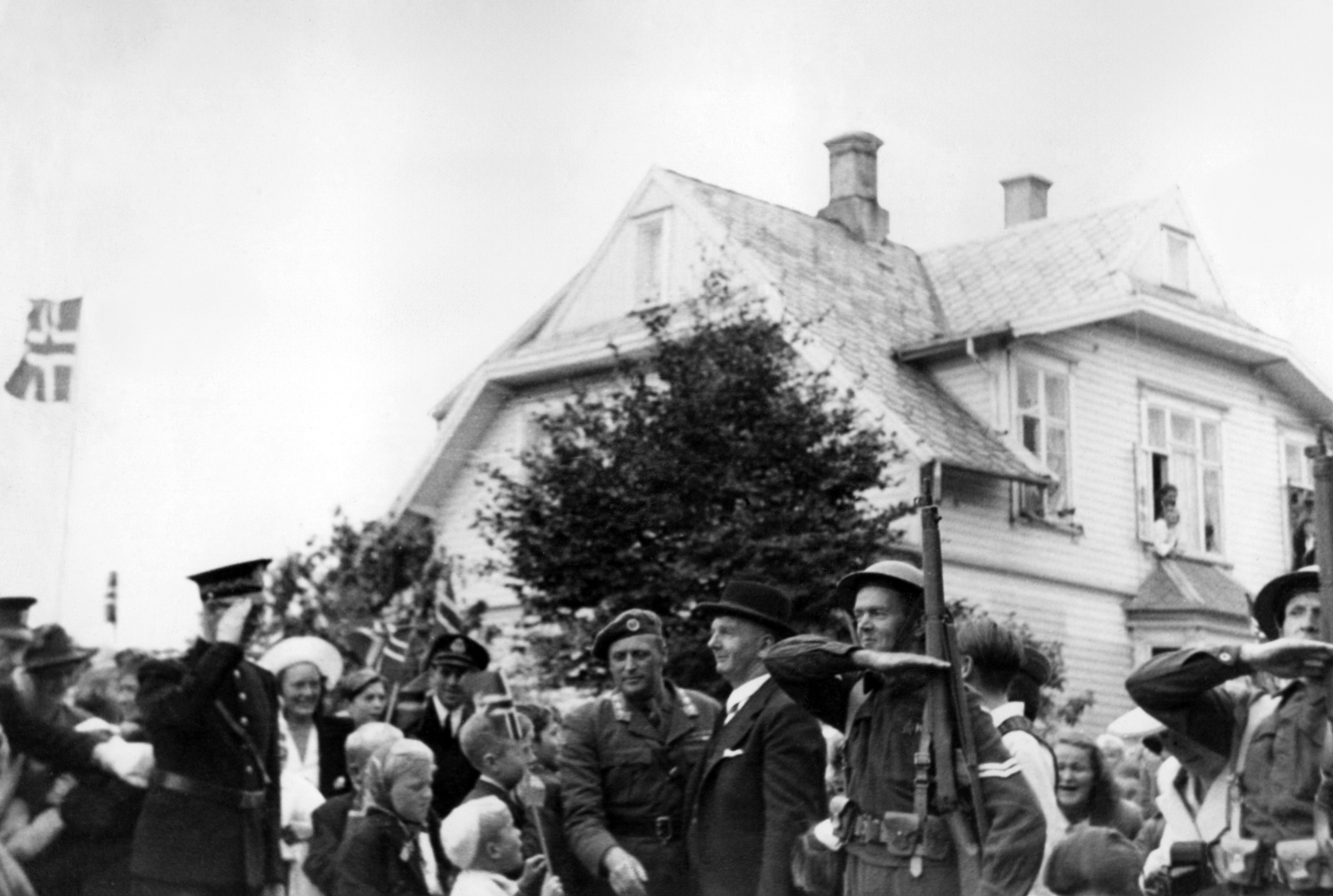 Kronprins Olav besøker Haugesund 29. juli 1945. Her ser vi også Haugesunds ordfører Christian Haaland og til høyre for ordføreren en smilende Sigmund Johannes Stangeland fra Kopervik. Sigmund Stangeland deltok i kamp i Ulvik og Kinsarvik. Unngikk å havne i krigsfangenskap. Han tjenestegjorde som Korporal ved Haugesundskompaniet/IR 8, fra 27.03.1940 til 01.05.1940. Soldat nr 11581/37. Dimittert ved Lillesund skole 2 mai 1945. Og har fått tildelt deltakermedaljen for sin innsats i 2 verdenskrig."""